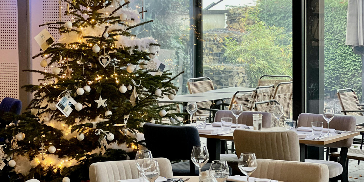 Christmas tree adorned with festive decorations and lights in a dining area, enhancing holiday ambiance for guests in a restaurant setting.